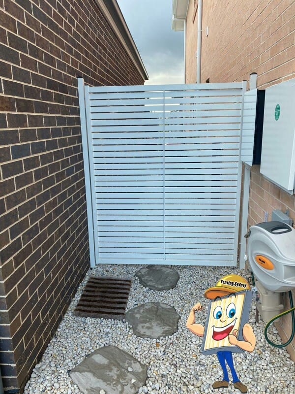 Two white aluminium horizontal slat gate leaves closing a narrow side passage between a brick house wall and a rendered wall