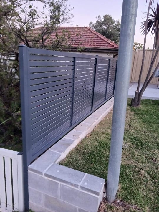 Charcoal aluminium horizontal slat fence panels mounted on top of a rendered block retaining wall beside a driveway