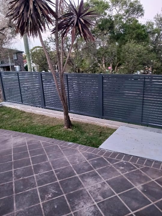 Run of charcoal aluminium horizontal slat fence panels along a garden boundary with a lawn and cordyline in the foreground