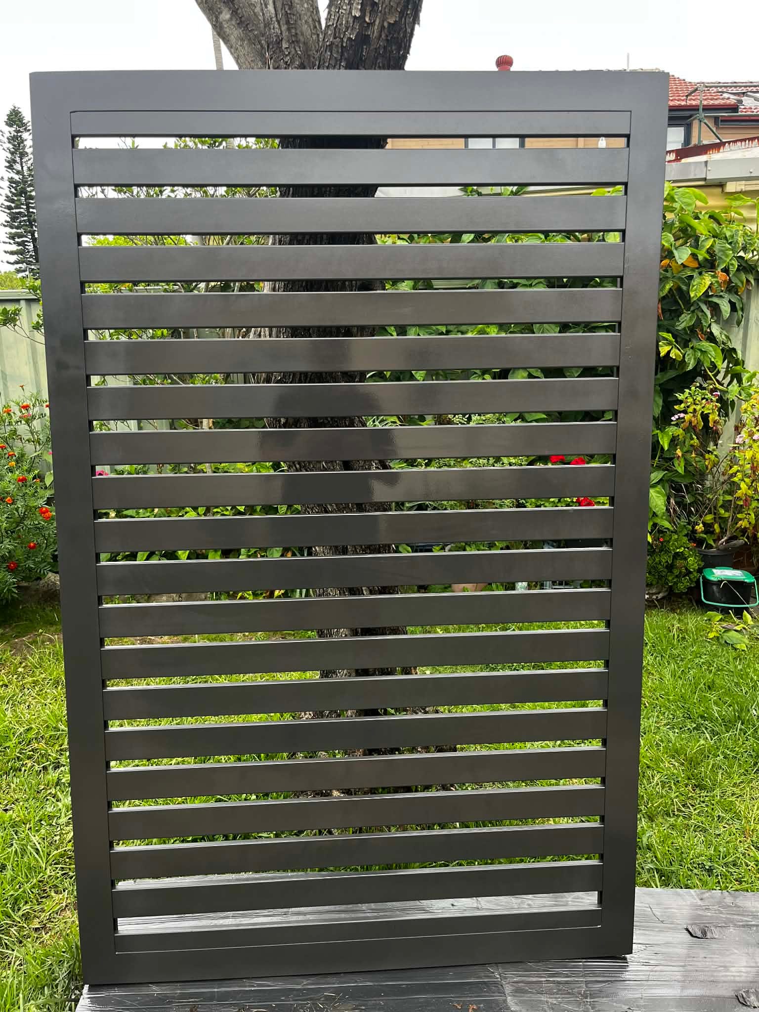 Newly fabricated black aluminium horizontal slat gate leaf standing upright on grass before installation