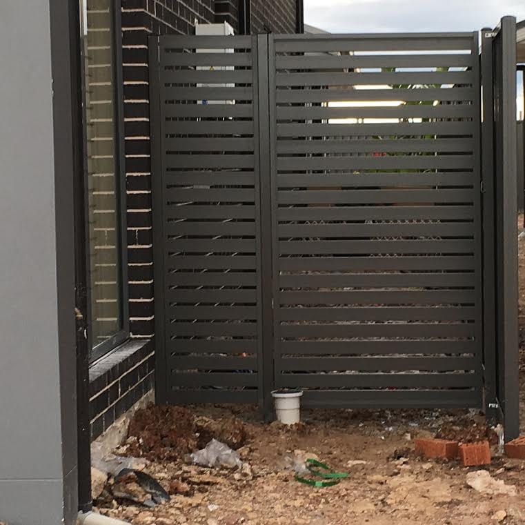 Charcoal aluminium horizontal slat gate installed next to a matching fixed slat panel against a dark brick wall