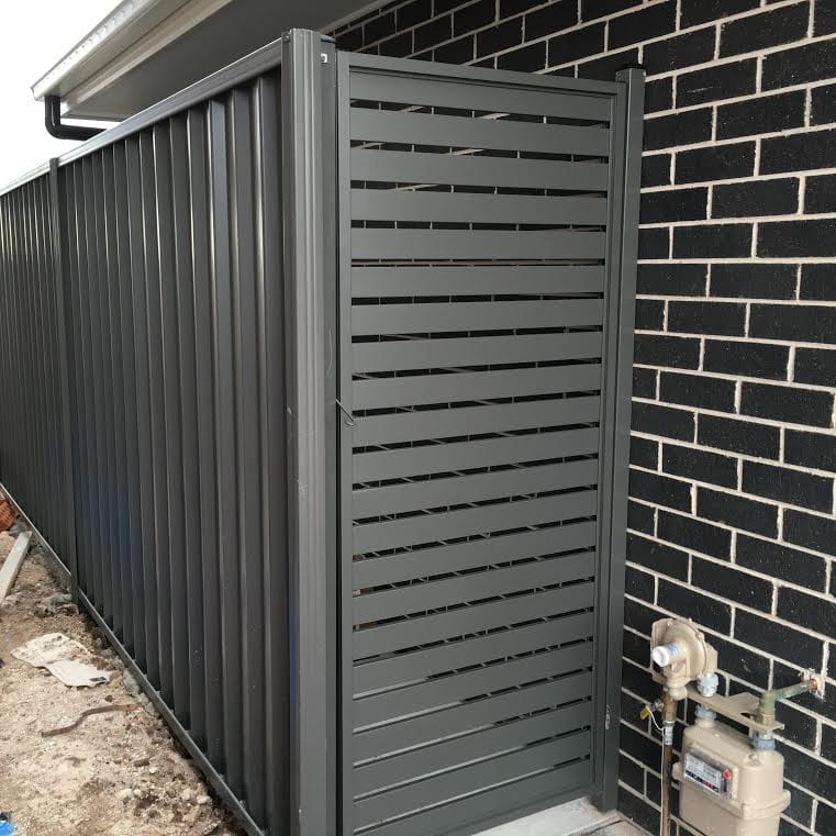 Dark grey aluminium horizontal slat gate installed beside a matching dark grey Colorbond fence and black brick wall