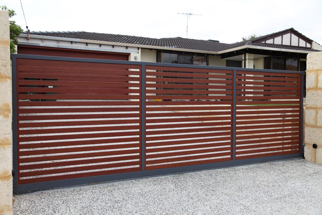 Woodgrain-finish aluminium horizontal slat sliding gate with a charcoal frame closed across a driveway between rendered piers