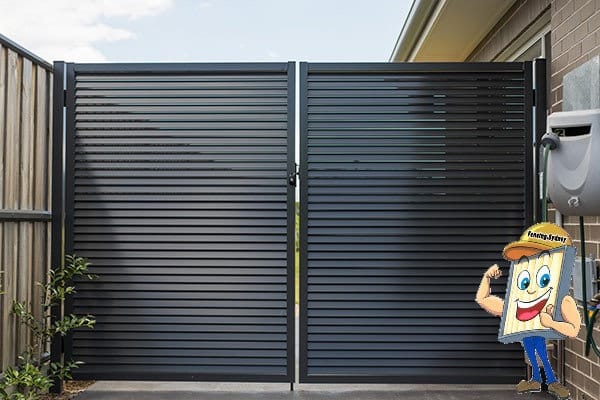 Pair of charcoal aluminium louvre gates closed across a driveway beside a brick house, with angled louvre blades