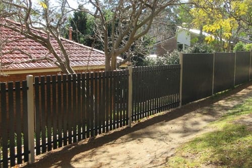 Dark bronze aluminium vertical picket fencing running along a boundary in front of a tiled-roof house
